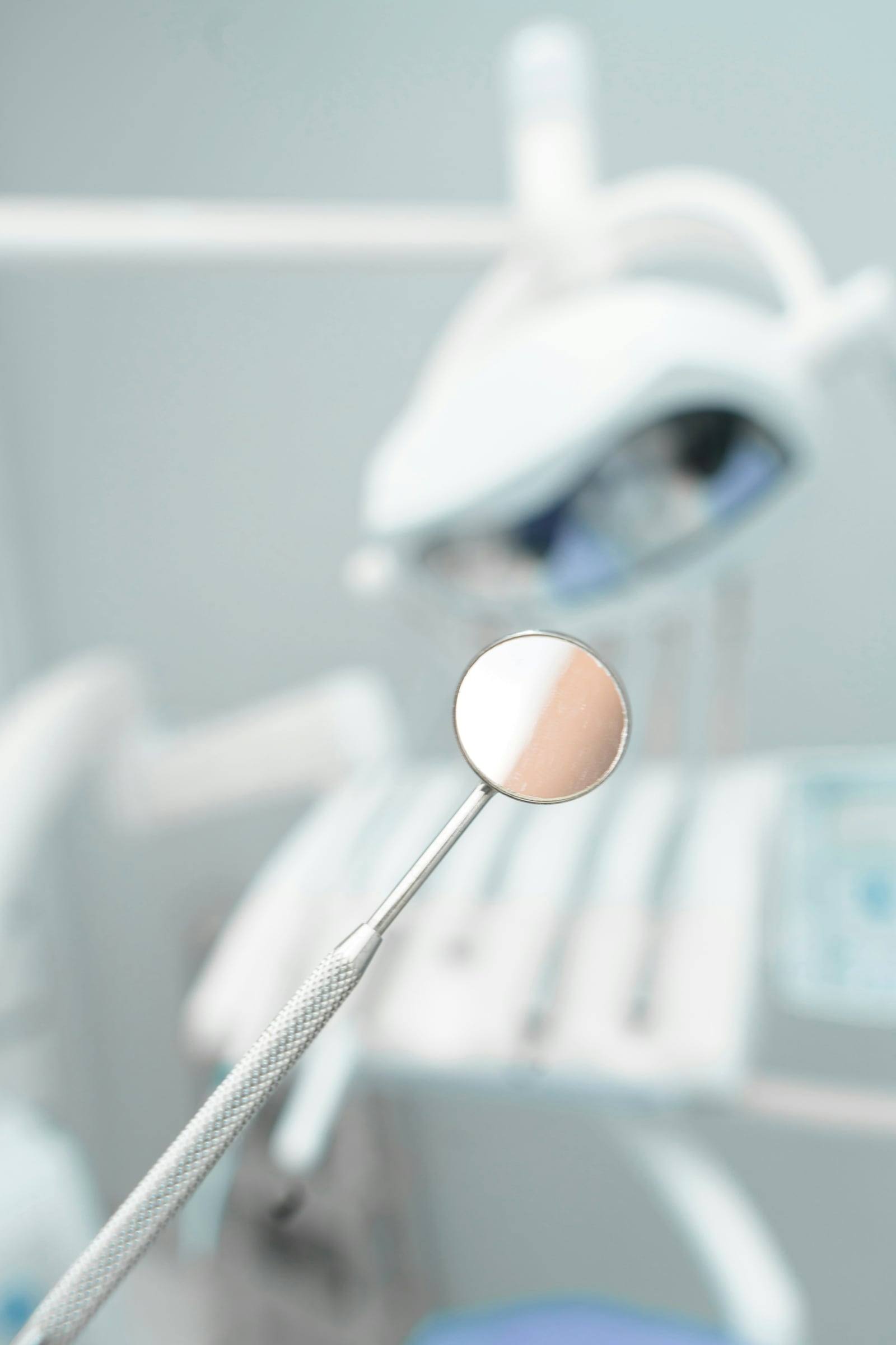 A dental mirror held up in a bright treatment room.